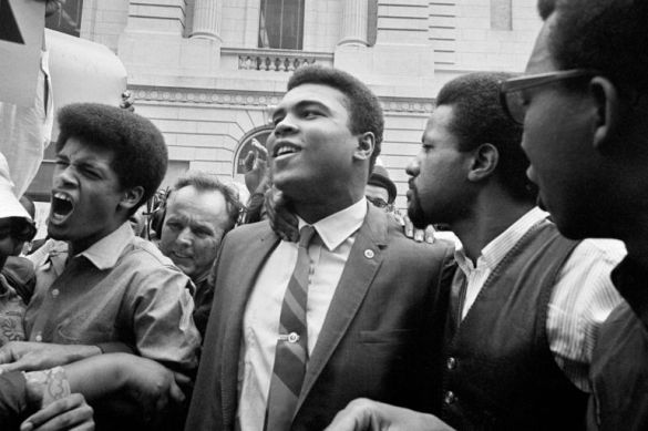 Heavyweight champ Muhammad Ali, center, leaves the Armed Forces induction center with his entourage after refusing to be drafted into the Armed Forces in Houston, April 28, 1967. Hundreds of Ali fans and supporters filled the streets to greet him when he left the building. (AP Photo)